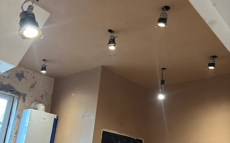 Freshly skimmed ceiling with six new downlights, and a boiler on an unplastered wall beside the window