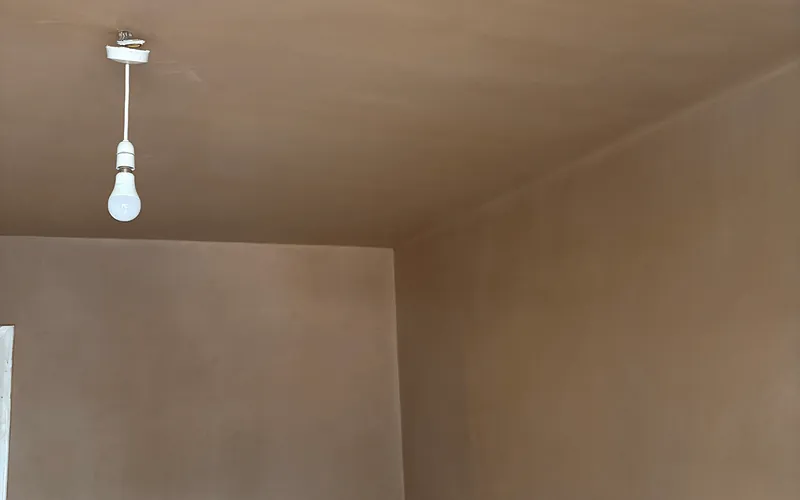 Freshly skimmed walls and ceiling in an empty room, with a bare bulb hanging from the ceiling
